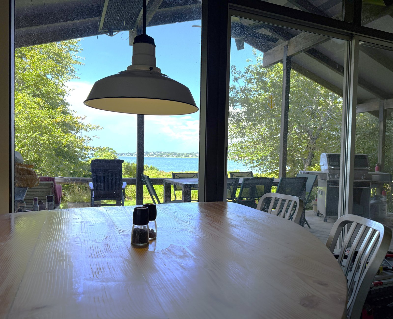 view of and from the indoor dining table, showing the outside deck, meadow, and Lake Monauk