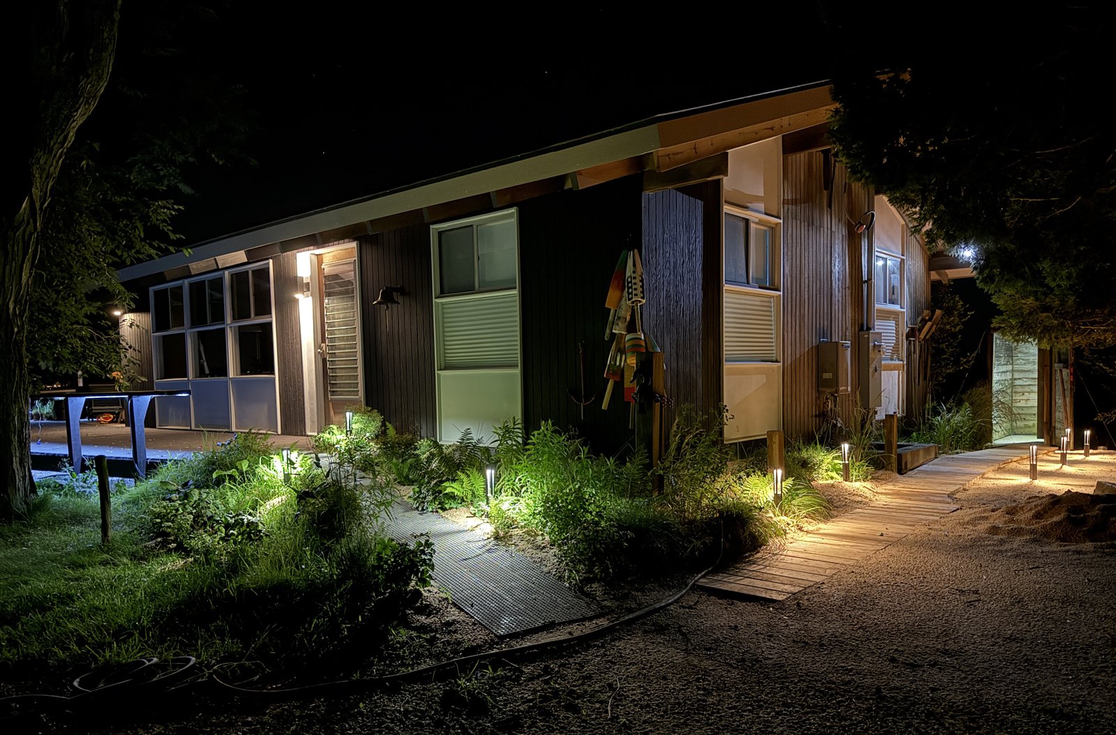 house exterior at night, showing deck, deck lighting, boardwalk to outdoor shower, lighting alongside boardwalk, and outdoor shower itself which is also lit