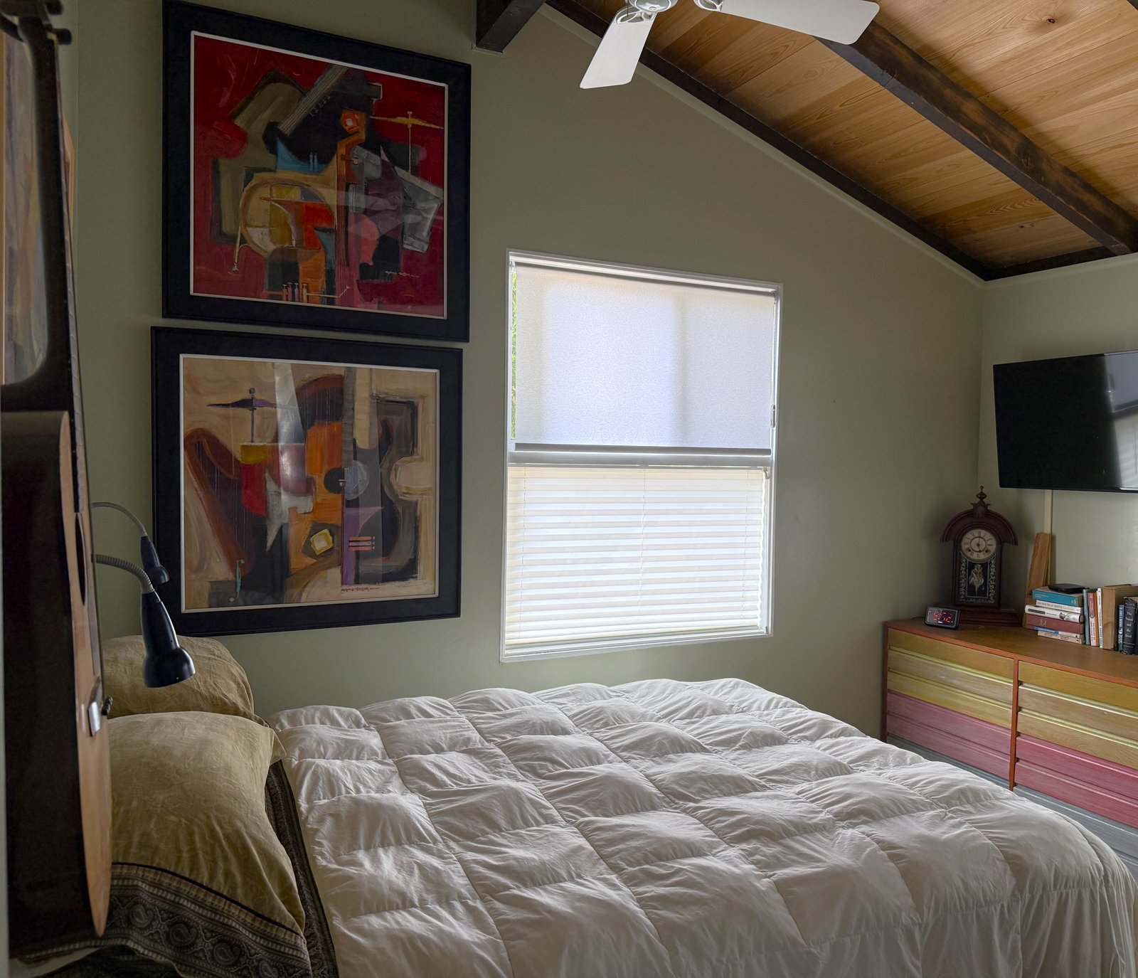 front bedroom showing bed, artwork, dresser, books, guitar hanging on wall, under ceiling fan with cypress sloped ceiling
